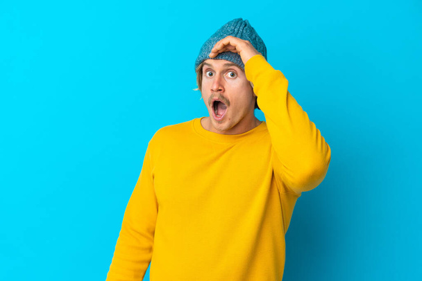 Handsome blonde man isolated on blue background doing surprise gesture while looking to the side - Фото, изображение