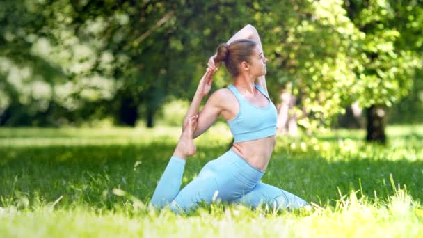 Mujer joven rubia realiza yoga asana Cabeza de vaca en parque - Imágenes, Vídeo