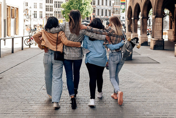 Back view of four friends hugging and walking in city center - urban lifestyle - Photo, image
