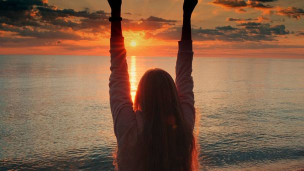Θαυμάζοντας την ανατολή του ηλίου στην ακρογιαλιά γυναίκα σηκώνει τα χέρια της - Φωτογραφία, εικόνα