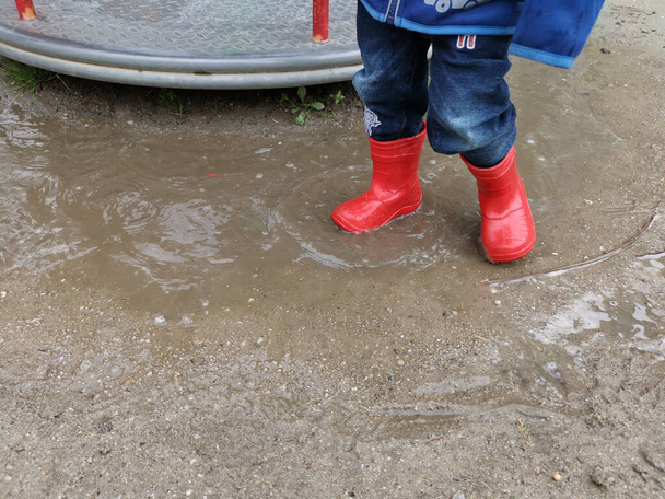 A closeup shot of a kid wearing red shoes and standing in a puddle - Fotografie, Obrázek