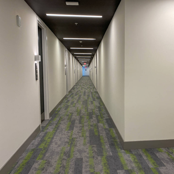 Un corridoio sterile con pareti bianche e tappeto a strisce grigie in un condominio senza nessuno intorno. - Foto, immagini