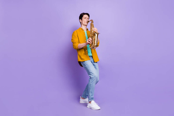 Full body photo of cool brunet young guy play sax wear brown shirt jeans isolated on violet color background - Foto, immagini