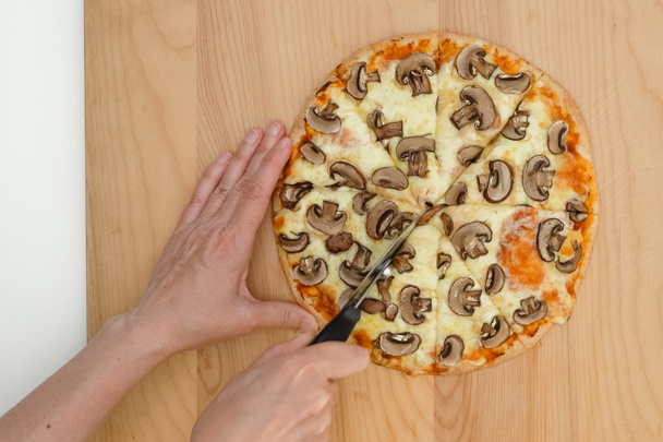Femme coupe une pizza aux champignons à l'aide d'un coupe-pizza, vue rapprochée d'en haut, fond en bois - Photo, image