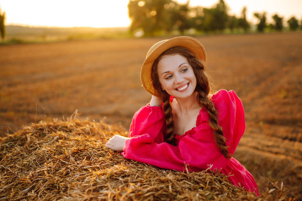  Beautiful curly woman in hat and clothes posing near hay bales in the countryside at sunset. Fashion concept. Nature, vacation, relax and lifestyle. - Fotoğraf, Görsel