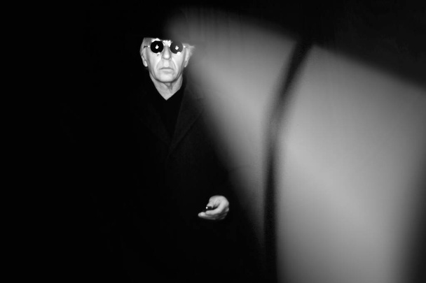 Griezelig beeld van een man in het zwart, met fedora hoed, lange jas en zonnebril op een donkere plaats. - Foto, afbeelding