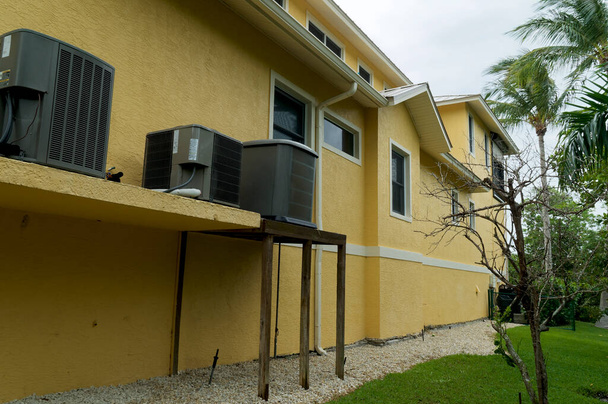 Florida 'daki palmiye ağaçlarıyla kaplı binanın dış tarafındaki hava kontrol birimlerini ya da klimaları gösteren uzun sarı ve beyaz bir bina. - Fotoğraf, Görsel