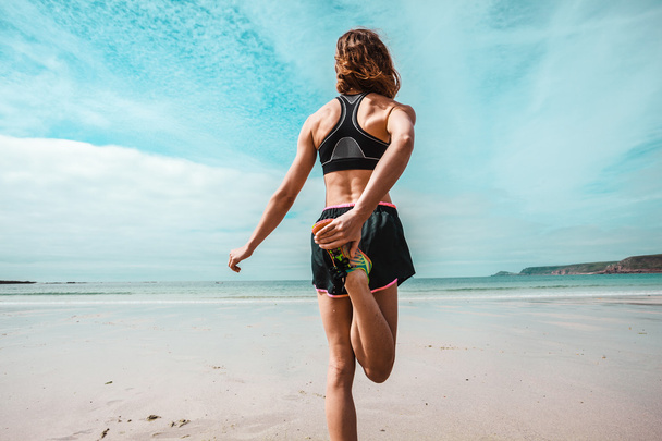 Athletic young woman stretching on the beach - Foto, Imagen