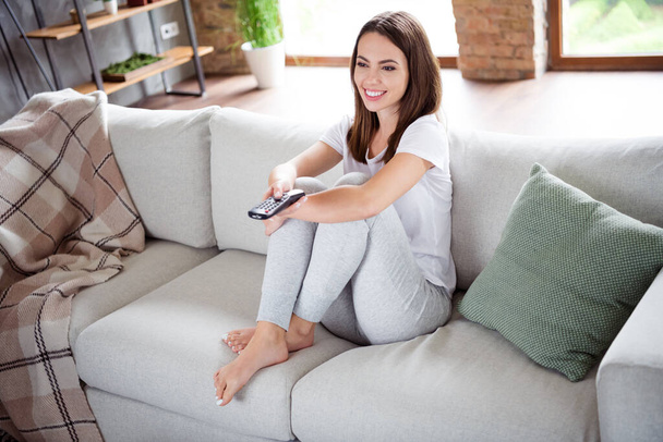 Photo portrait brunette woman sitting on sofa at home smiling watching tv with remote controller - Fotó, kép