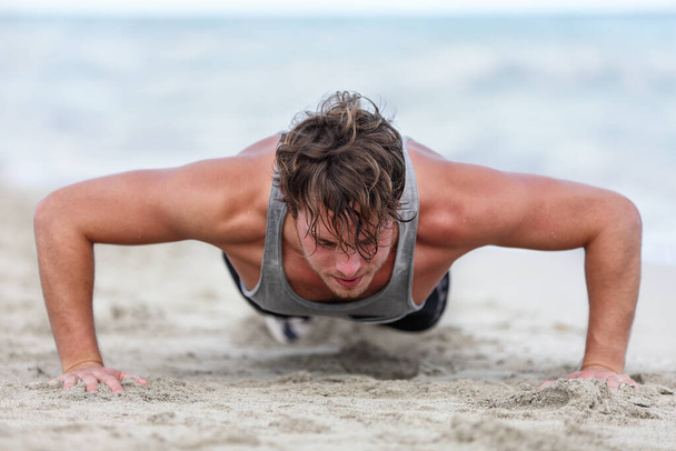 Fit fitness man exercising arms muscles doing exercise push ups exercises. Caucasian male fitness athlete model cross-training push-up on beach outdoor. Pushups trainer working out in summer on beach. - Фото, изображение