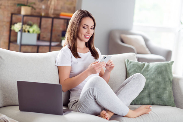 Täysikokoinen kuva houkutteleva nuori nainen istua sohvalla katso pidä puhelimen sosiaalisen median sisällä talossa kotiin - Valokuva, kuva