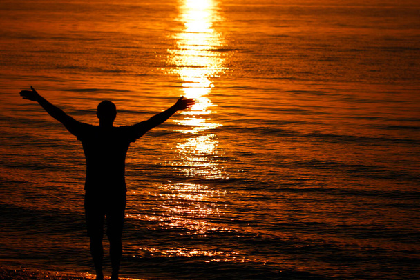 Силует чоловіка, що піднімає руки або відкриває руки, коли сонце сходить над морем
. - Фото, зображення