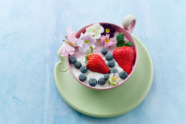 A green cup of ice cream with strawberries and blackberries on the blue background - Foto, afbeelding
