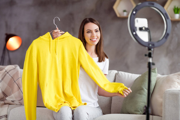 Photo of young attractive girl happy positive smile make video blogging demonstrate jumper hoodie ad home - Foto, Imagen