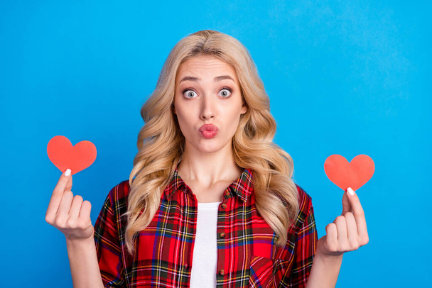 Photo of flirty adorable young lady wear plaid shirt holding two red hearts lips pouted isolated blue color background - Фото, зображення