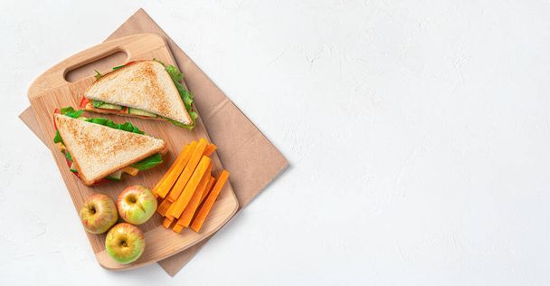 Los bocadillos, las manzanas y las zanahorias sobre la tabla sobre la bolsa kraft sobre el fondo gris. Preparación de un almuerzo escolar. - Foto, imagen