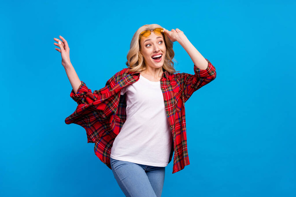 Photo of adorable excited woman dressed checkered shirt glasses dancing looking empty space smiling isolated blue color background - Fotoğraf, Görsel