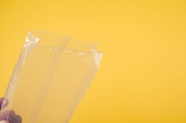 A closeup shot of a man's hand keeping a plastic bag on a yellow background - Zdjęcie, obraz