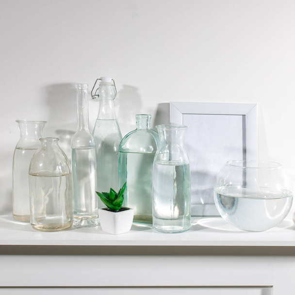 A set of water bottles of different shapes with a photo frame and a pot with artificial succulent is on the dresser. Copy space - Valokuva, kuva