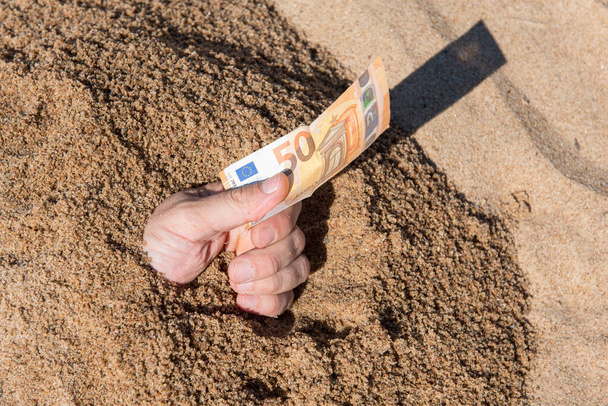 Vijftig euro in de hand van een man die uit het zand steekt - Foto, afbeelding