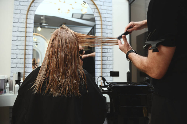 Ein Friseur kämmt die langen, feuchten Haare einer Kundin eines Schönheitssalons und schneidet die Haarenden, um die Länge auszugleichen. - Foto, Bild