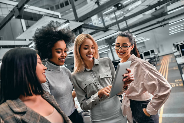 A group of young successful business women working together standing in the middle of the office and looking at a tablet. - Fotografie, Obrázek