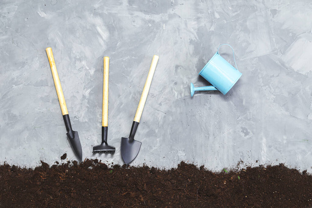 Tuingereedschap - schoffel, schep, gieter en bodem op een grijze achtergrond. Tuinieren en tuinbouw.  - Foto, afbeelding
