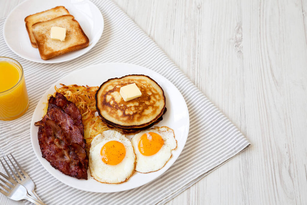 Full American Breakfast with Bacon, Hash Browns, Eggs and Pancakes on a plate on a white wooden background, side view. Space for text. - Photo, Image