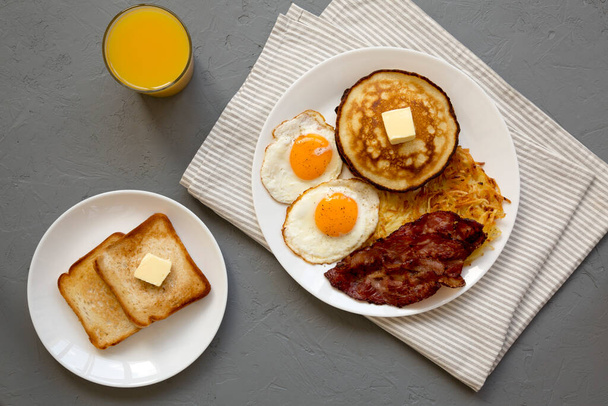 Full American Breakfast with Bacon, Hash Browns, Eggs and Pancakes on a plate on a gray background, top view. Overhead, from above, flat lay. - Photo, Image