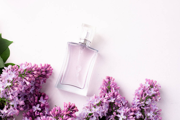 Una botella de perfume y lila sobre un fondo blanco. Perfume de mujer. Fragancia de primavera. Aromaterapia. Bonito olor. Belleza y moda. Artículo sobre la elección de la fragancia. Un artículo sobre corriente - Foto, imagen