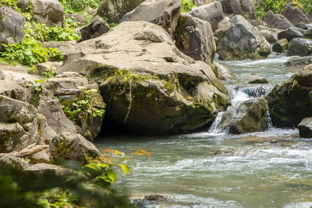 Um rio sinuoso de montanha flui entre as pedras entre as rochas e a floresta, uma cachoeira e corredeiras de água tempestuosas. - Foto, Imagem