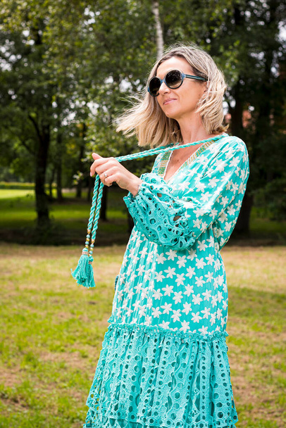 Blonde model poseren in een mooie lange groene jurk en zonnebrillen.De foto is genomen op een zonnige dag in een park in Asturië, Spanje.De foto is genomen in verticale vorm. - Foto, afbeelding