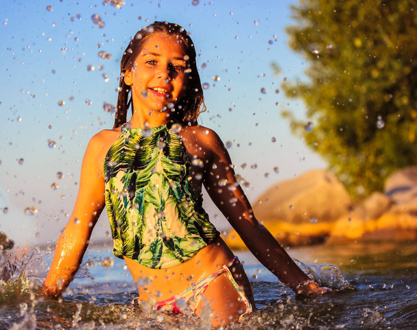 Beautiful smiling happy teenage girl frolicking in a sea at summer. Splashing, dripping water. A cute kid at a children's camp on summer holiday have fun outdoors. Childhood concept. Positive emotions - Photo, Image