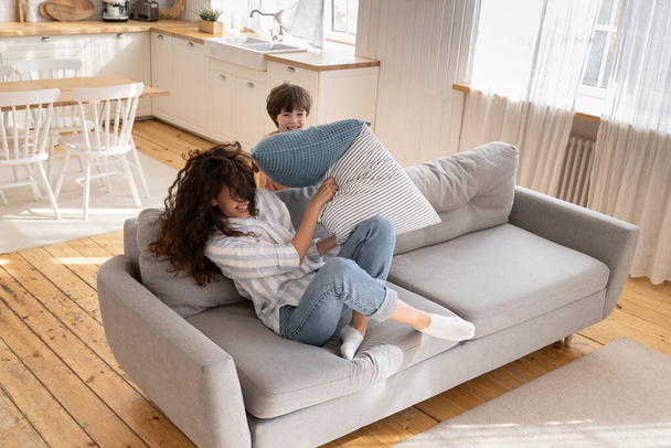 Laughing single mom and little son have fun together happy play childish pillow fight in living room - Foto, Imagem