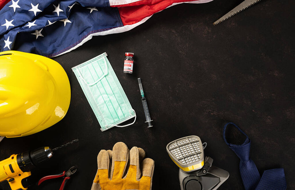 Happy Labor Day. Several engineer constructor work tools, medical face mask protective and American flag with copy space black dark background, American workforce during breakout coronavirus concept - Photo, Image