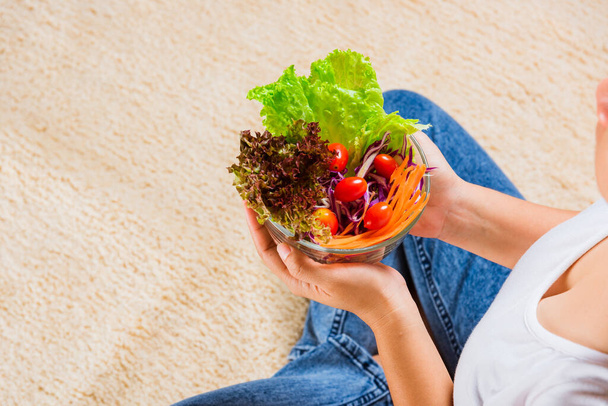 Young woman eating fresh salad meal vegetarian spinach in a bowl, top view of female hands holding bowl with green lettuce salad on legs, Clean detox healthy food concept - Φωτογραφία, εικόνα