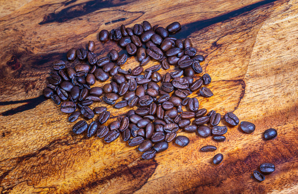 Top view close up to a heap fresh roasted coffee beans on a wooden background. High resolution detailed macro picture on brown roasted coffee beans on tropical wood table. Background  wallpaper image - Photo, Image