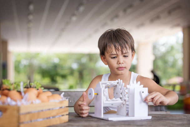 Un garçon et prêter attention à l'apprentissage du modèle de robot de mécanisme de simulation en bois sur la table à la maison. - Photo, image