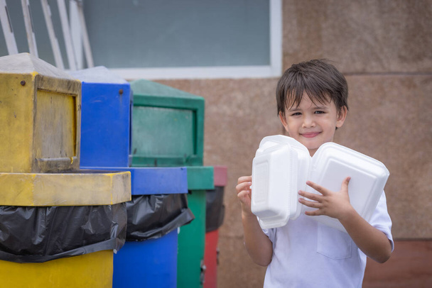 Een jongen die de piepschuimdoos in de vuilnisbak bewaart.Styrofoam dozen voor afhaalmaaltijden thuis veroorzaken vervuiling en kunnen niet hergebruikt worden. - Foto, afbeelding