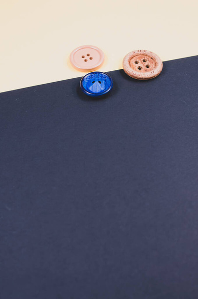 A flat lay of different sizes of sewing buttons on a beige and dark background - Foto, Bild