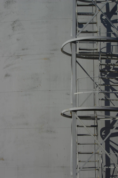 A vertical shot of a ladder on the side of a large white tank on an oil refinery plant - Фото, зображення