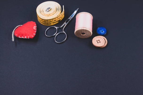 A flat lay of scissors, measuring tape, buttons, cushion, and thread on a dark background with free space for text - Valokuva, kuva