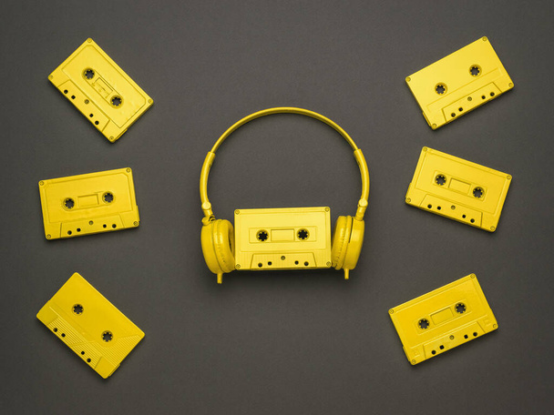 暗い背景に散乱黄色のテープカセットと黄色のヘッドフォン。色のトレンド。音楽を聴くためのヴィンテージ機器。平敷. - 写真・画像