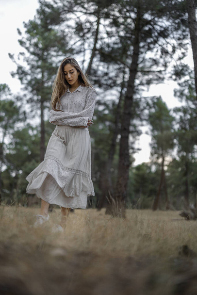 An adult Spanish woman wearing a white dress and walking in a meadow on a gloomy day - Fotoğraf, Görsel
