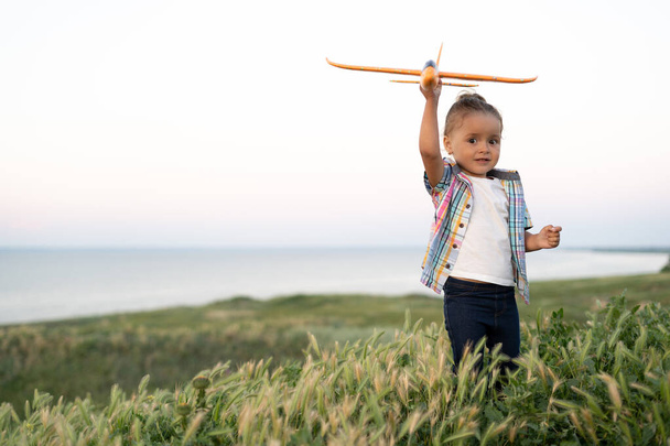 A kislány felrepít egy játékrepülőt az égbe. A baba nyáron sétál a mezőn naplementekor. gyermekkor és egészséges életmód koncepció. - Fotó, kép