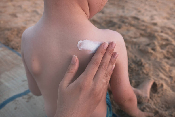 Μητρικό χέρι που απλώνει αντηλιακή κρέμα προστασίας σε μικρό παιδί. SPF αντηλιακό κατά τη διάρκεια των καλοκαιρινών διακοπών στη θάλασσα, έννοια φροντίδας του δέρματος. Κλείσε. - Φωτογραφία, εικόνα