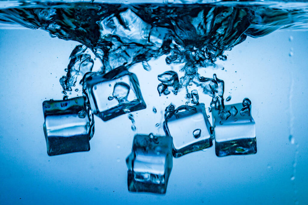 primer plano de cubos de hielo en gotas de agua sobre fondo azul, espacio de copia - Foto, imagen