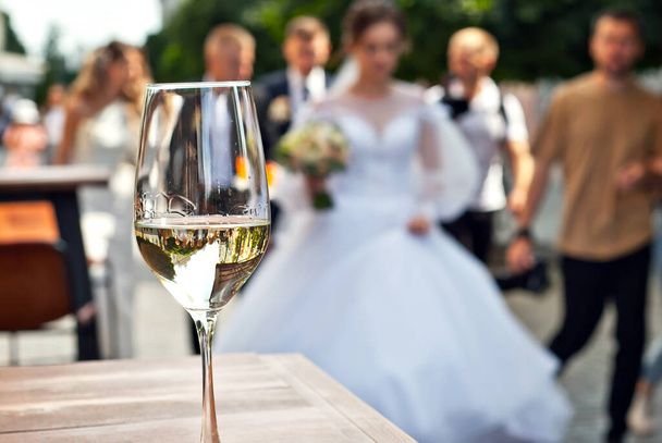 Glass of white wine close up. Alcoholic drink on a wooden table on a background of the city. Transparent wine on the summer terrace of the restaurant. Blurred people in the background. - Foto, imagen