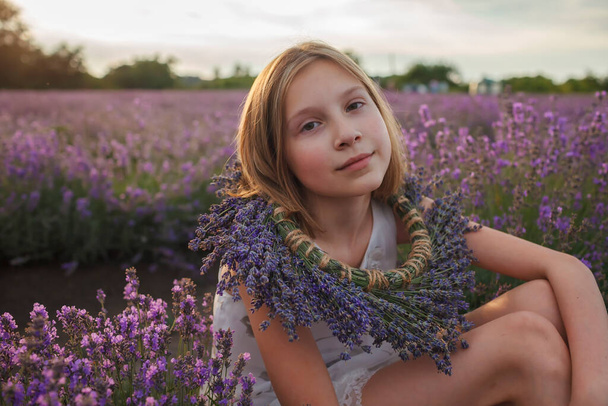 Marzycielska nastolatka z kwiatowym wieńcem siedzi na lawendowym polu. Piękno natury, letni styl życia - Zdjęcie, obraz