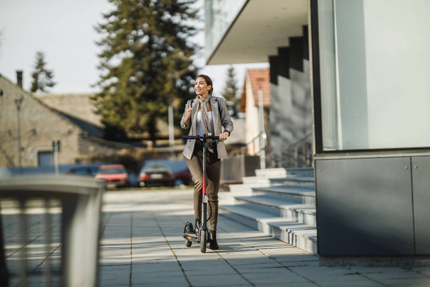 Una joven empresaria montando un scooter eléctrico camino al trabajo. - Foto, imagen